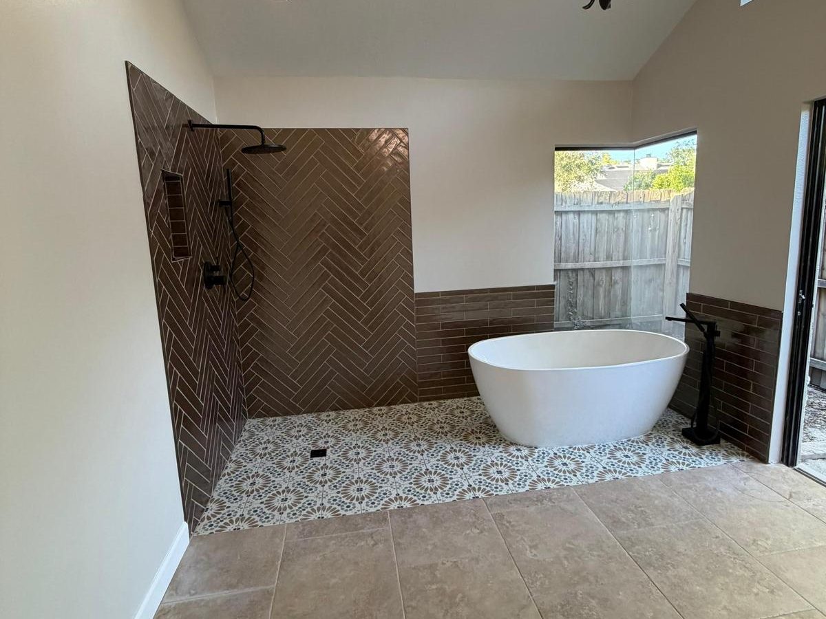 Renovated primary bathroom with herringbone tile walk-in shower, patterned floor tile and a freestanding tub