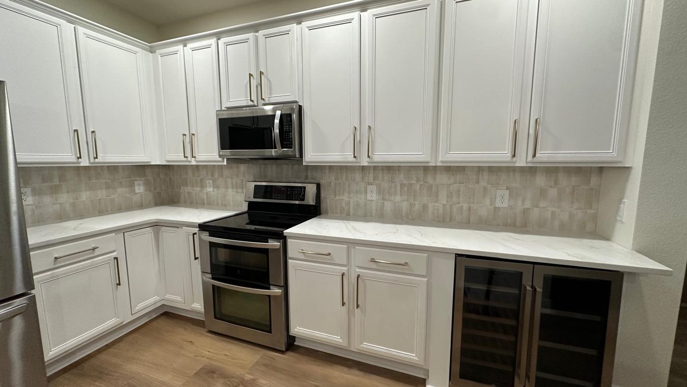 Kitchen cabinets painted bright white with brushed gold pulls, marble-look counters and tile backsplash