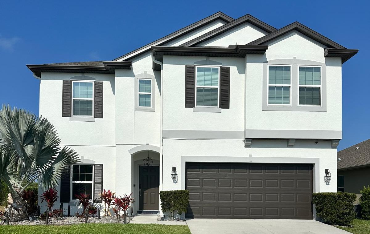 Two-story Florida stucco home freshly painted white with dark brown shutters, trim and garage door