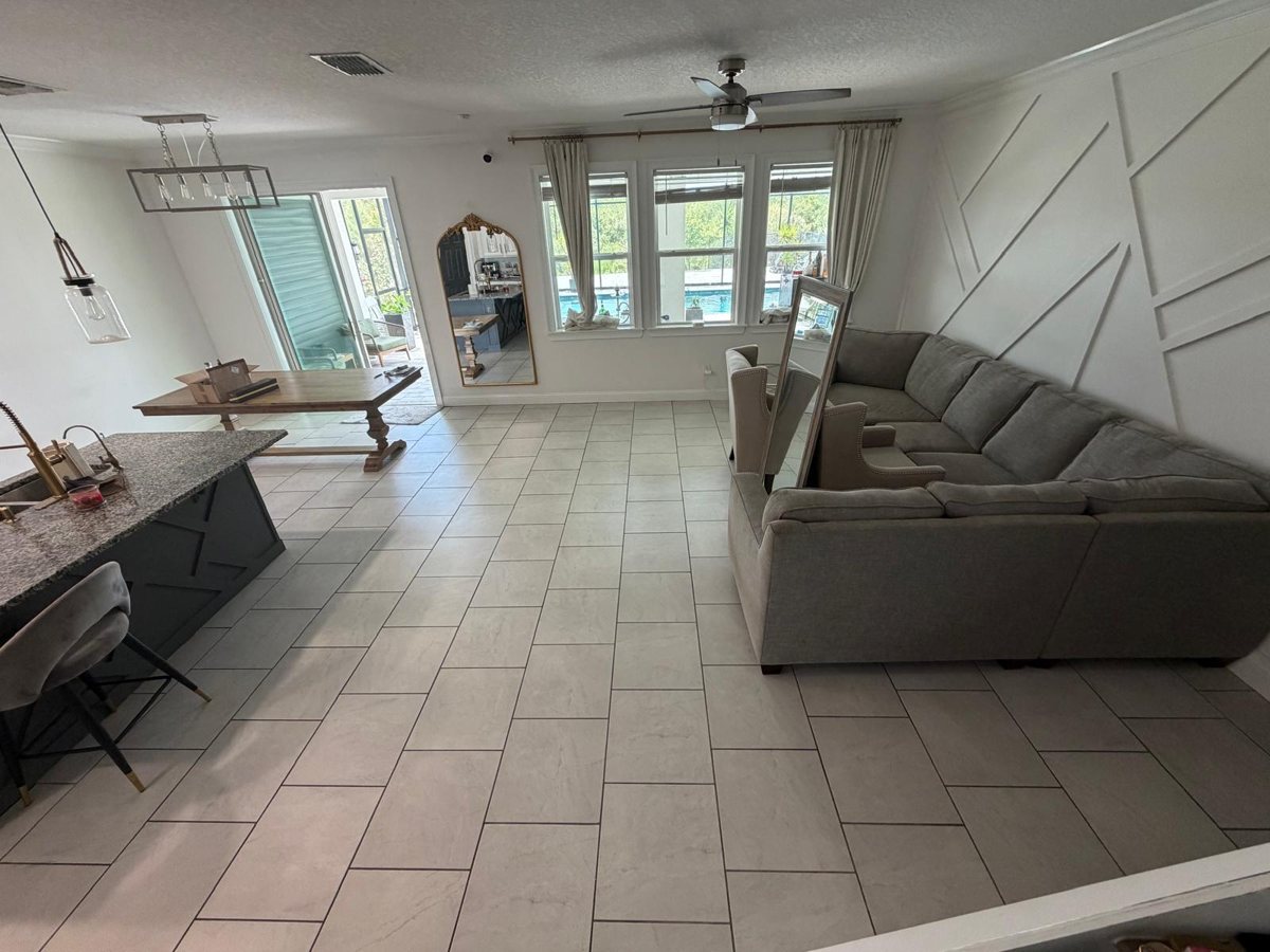 Open living area with gray tile replaced by warm wood-look laminate flooring — before