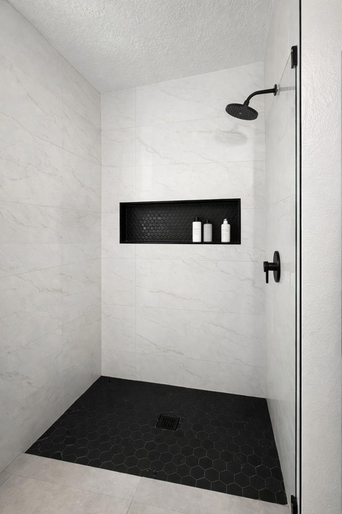 Finished walk-in shower with marble-look tile, black hex floor and matte black fixtures